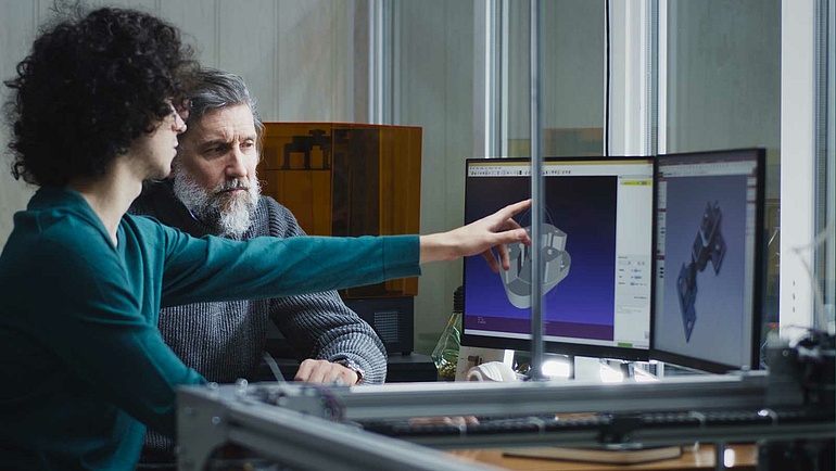 Zwei Männer betrachten ein digitale Modell eines Werkstück auf zwei Computermonitoren.