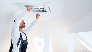 Ein Klimaanlagentechniker birngt die Abdeckung einer Klimaanlage an einer Decke an.