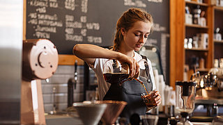 Frau im Cafe gießt Kaffee ein
