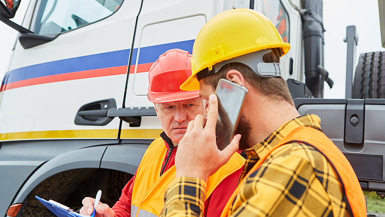 Bauarbeiter mit Handy und Checkliste kontrollieren LKW